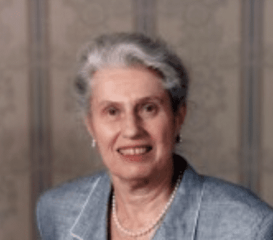 Senior woman with grey hair pulled back in a bun. Smiling. Blue grey top.